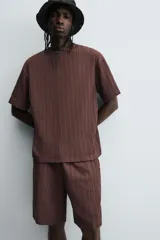 Bermuda de corte relajado color marrón oscuro, confeccionada en tejido jacquard con textura acanalada vertical. Presenta cintura elástica ajustable con cordón, bolsillos delanteros y un bolsillo trasero de plastrón.