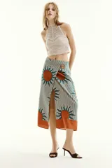 Falda midi estilo pareo con diseño cruzado, estampado de rayas verticales en tono verde oscuro y blanco, combinado con grandes motivos de soles naranjas y verdes, y cierre lateral con botón.