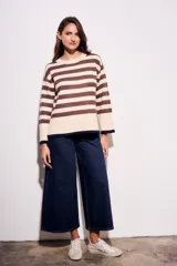 Sweater de punto a rayas horizontales negras y crudas, con cuello redondo y mangas largas. Tiene ribete marrón en puños y ruedo.