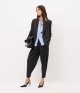 Pantalón de sastre de corte wide leg con diseño de rayas verticales, confeccionado en crepé color gris oscuro. Cuenta con tiro alto, pinzas profundas en el frente y detalle de tira ajustable con botón en el ruedo.