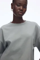 Remera gris de corte cuadrado y holgado, con cuello redondo y mangas cortas anchas. Confeccionada en tejido de punto suave de algodón.