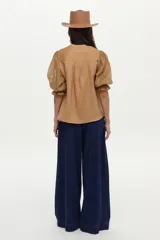 Blusa color tostado confeccionada en lino, con mangas abullonadas de ramie y detalles de bordado en punto smock en los puños.