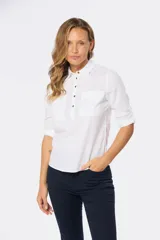 Camisa blanca de manga larga con cuello y tapeta de medio botón. Presenta dos bolsillos frontales con tapa y botones metálicos. Las mangas tienen presillas para sujetar el puño enrollado.