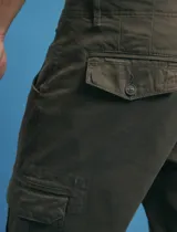 Pantalon cargo de corte recto en color verde militar, confeccionado en sarga de algodón con elastano. Presenta bolsillos laterales con fuelle y tapa, además de bolsillos traseros con cierre de botón.