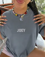 Remera oversize gris oscuro con corte holgado, mangas cortas y estampa trasera en blanco y negro con forma de estampilla que muestra a una persona con un gato y el texto 'Kaboa Industries'.