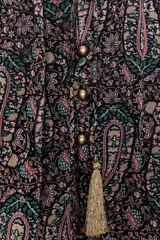 Blusa semitransparente con estampado paisley en tonos rosa, verde y beige sobre fondo negro. Presenta cuello redondo con escote en pico y lazada con borlas doradas. Tiene manga larga y cierre frontal con botones. Incluye forro interior.