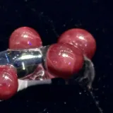 Anillo artesanal de vidrio transparente con diseño irregular y esferas de vidrio color bordó integradas en la estructura.