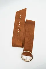 Cinturón ancho de gamuza color marrón, con hebilla circular grande de metal dorado y ojales metálicos a lo largo de la tira.