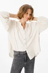 Camisa de corte holgado y silueta oversize, color beige, con cuello mao, cierre frontal de botones y mangas largas abullonadas con puños elásticos.