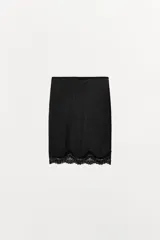 Falda tipo media de tiro medio y cintura elástica, color negro. El bajo está acabado con una aplicación de encaje combinado a tono.