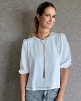 Remera blanca de algodón con cuerpo de tejido liso y mangas abullonadas de textura diferenciada. Presenta cuello redondo con costuras decorativas y ruedo con detalle de pespunte a tono.