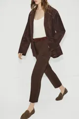 Pantalón de tiro alto en color beige, con diseño de pinzas frontales y bolsillos laterales. Incluye un cinturón a contraste en tono marrón con hebilla metálica y cierre frontal con cremallera y gancho.