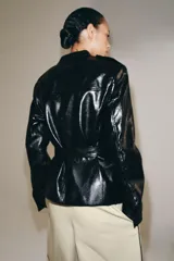 Cazadora efecto piel de Zara Woman Collection, en color negro. Cuenta con cuello redondo, manga larga, bolsillos de parche con solapa en el delantero y cierre frontal con botones forrados. Incluye un cinturón del mismo tejido para ajustar en la cintura.