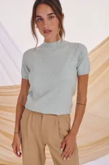 Polera de tejido de punto color celeste claro, de manga corta y cuello alto tipo mock neck.