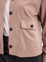 Campera de pana color beige, con cuello camisero, cierre frontal de botones oscuros, mangas largas con puños abotonados y dos bolsillos frontales con solapa.