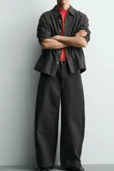 Pantalón de corte relajado confeccionado en tejido de algodón. Presenta cintura con trabillas laterales ajustables, bolsillos frontales y traseros, y un diseño distintivo de costuras laterales giradas que recorren la pernera.