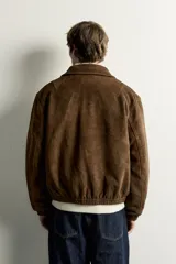 Cazadora de hombre regular fit confeccionada en tejido efecto ante, con acabado lavado, cuello solapa, manga larga, bolsillos de plastrón con solapa en la cadera, detalles elásticos en puños y cintura, y cierre frontal de cremallera.