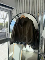 Campera de gamuza color verde militar, con corte oversize, cuello camisero, cierre frontal y mangas amplias con puños ajustados.