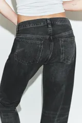 Jeans rectos de tiro medio en denim negro con efecto lavado. Presenta diseño de cinco bolsillos, trabillas para cinto y bajo con vuelta marcada. Cierre frontal con botones metálicos ocultos.