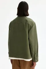 Sobrecamisa de lona de algodón en color verde militar, con cuello clásico, cierre frontal de botones y tres bolsillos de parche frontales. Presenta mangas largas con puños abotonados y un diseño de corte recto.