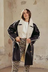 Cazadora larga de estilo doble faz, confeccionada en cuero sintético negro con interior de corderito sintético color crema. Presenta un diseño de corte recto, cierre frontal con botones, solapas amplias y bolsillos laterales.