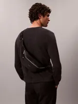Riñonera Calvin Klein de poliuretano texturizado color negro, con cierre superior de cremallera y un bolsillo frontal con cierre. Cuenta con correa ajustable y detalles metálicos plateados.