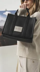 Cartera estructurada de tamaño mediano, confeccionada en símil cuero color negro. Presenta doble asa de mano, correa larga ajustable y desmontable, y un bolsillo trasero con cierre. El compartimento principal cuenta con cierre, división interna y bolsillos organizadores.