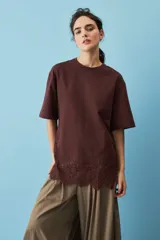 Remera blanca de algodón, de corte oversize, manga corta y cuello redondo, con detalle de aplique de encaje floral en el borde inferior.