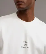 Remera boxy de algodón color crudo, con cuello redondo y mangas cortas. Estampa frontal con la frase "l'ami du contraire" y estampa trasera de figuras estilo art noveau.