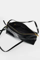 Bolso de hombro tipo baguette en color negro con acabado brillante. Presenta un diseño rectangular con cierre de cremallera superior y doble asa ajustable mediante hebillas metálicas.