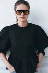 Camisa de algodón con cuello redondo, manga tres cuartos con puño elástico y volante. Presenta detalles de flores bordadas a tono, entredoses y cierre posterior con abertura y botón.