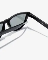 Lentes de sol Hawkers unisex, modelo One Raw, con montura cuadrada negra y lentes polarizadas color violeta.