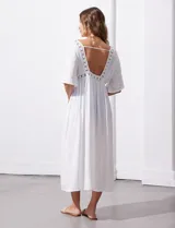 Kaftan largo de playa color blanco, con mangas cortas, escote en V y detalles de puntilla en el frente. Presenta una abertura central con lazo de ajuste en la cintura.