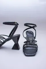 Sandalias de tacón geométrico con diseño de tiras finas lisas y trenzadas que se entrelazan en el empeine y tobillo. Cuentan con cierre de pulsera ajustable y punta cuadrada.