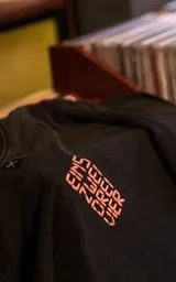 Remera de manga corta con cuello redondo y calce oversize, color negro con efecto lavado. Presenta un estampado frontal gráfico con motivos musicales y tipografía en tonos rojos y blancos.