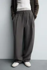 Pantalón de corte relajado, color gris oscuro, con cintura elástica ajustable mediante cordón y pliegues frontales. Presenta bolsillos laterales y bolsillos traseros de parche con pespuntes contrastantes.