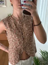 Chaleco de lino estampado con diseño ikat en tonos marrón y crudo, sin mangas, con cuello redondo y cierre frontal de botones tapados.