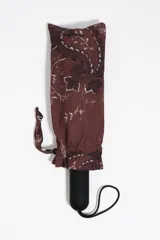 Paraguas plegable marrón con estampado gráfico blanco y negro, mango negro con relieve de la marca y funda a juego.