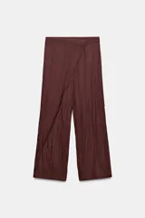 Pantalón de tiro medio con diseño tipo pareo, confeccionado en tejido satinado con acabado arrugado. Presenta pernera recta, cierre frontal con botón a presión y cremallera lateral oculta.