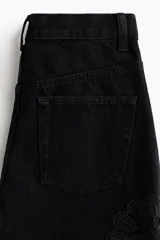Jean negro de cinco bolsillos en denim de algodón rígido, con perneras amplias, tiro alto y detalles de crochet tono sobre tono en los laterales.