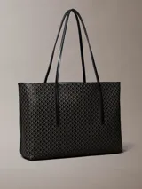 Cartera tote Calvin Klein de diseño estructurado, color negro y marrón con estampado de monograma CK en toda la superficie. Cuenta con asas de mano dobles y finas, y viene acompañada de una mini cartera lisa con cierre y detalle del logo de la marca en dorado.
