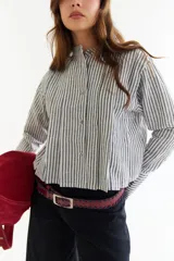 Blusa blanca de algodón con cuello mao y tablas verticales en el frente que crean un efecto de volumen. Presenta cierre frontal con botones y mangas largas.