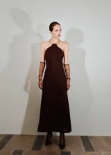 Vestido largo de corte evasé en color marrón, con cuello halter rígido metálico tipo choker. Presenta un diseño sin mangas y una caída fluida.