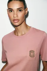Camiseta de algodón con efecto lavado, cuello redondo y manga corta. Presenta un detalle de fornitura metálica aplicada en el pecho.