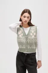 Chaleco tejido de punto con diseño jacquard de corazones y motivos geométricos en tonos verde y rosa. Presenta escote en V, cierre frontal con botones y terminaciones acanaladas en cuello, sisas y ruedo.
