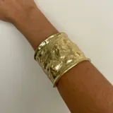 Brazalete ancho dorado con textura irregular.