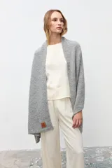 Chal abierto de tejido de punto en color gris, con textura suave y etiqueta de cuero sintético en el borde inferior.