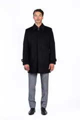 Abrigo negro de corte recto, largo hasta la rodilla, con cuello clásico, cierre frontal con un botón y bolsillos laterales.