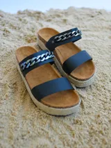 Sandalia de plataforma estilo alpargata, color negro, con dos tiras anchas sobre el empeine. La tira superior está decorada con una cadena gruesa plateada.