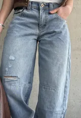 Jean de denim celeste de corte barrel, tiro bajo, con roturas y detalles desgastados en la rodilla.
